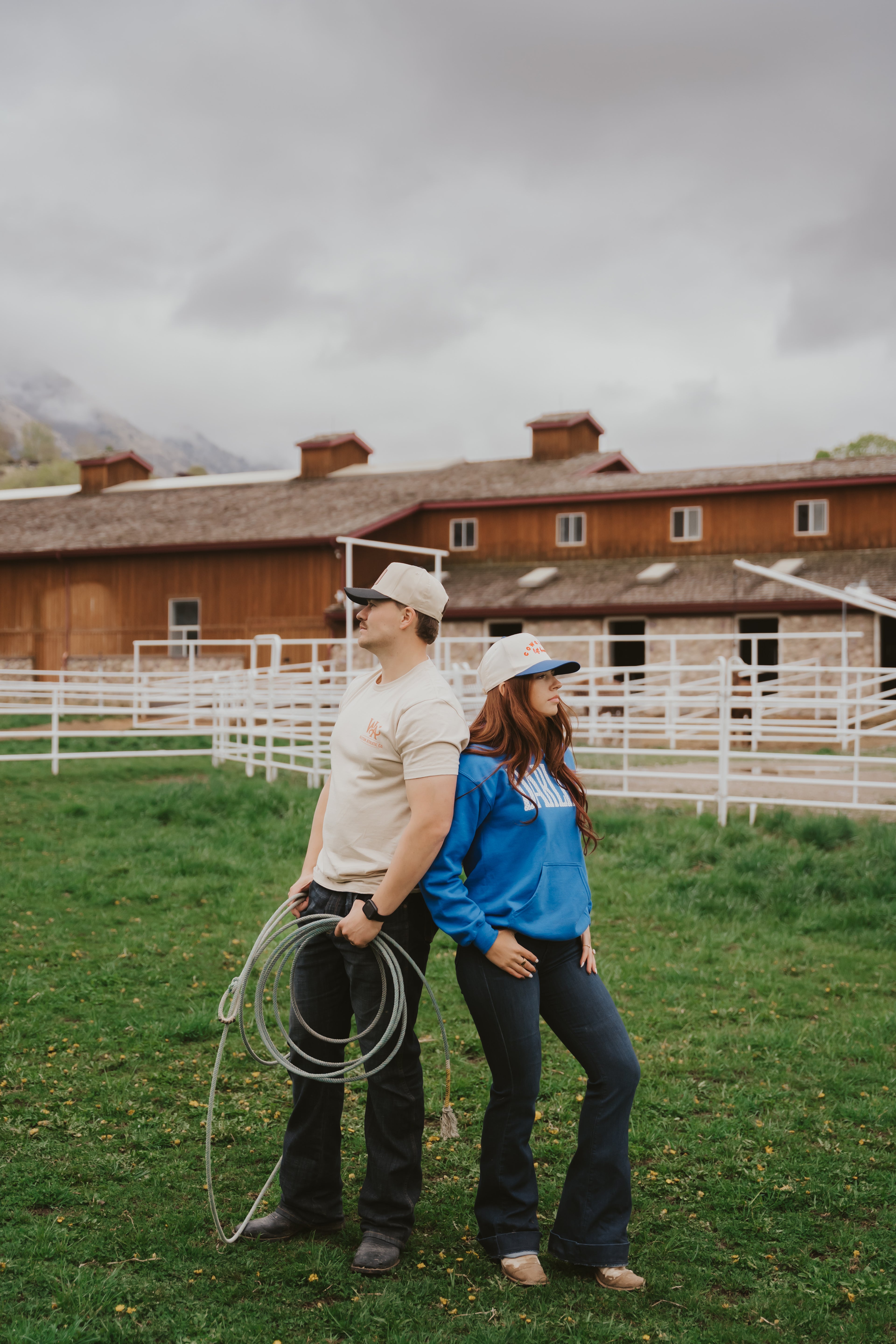 Two people standing in a grassy field with a wooden building in the background